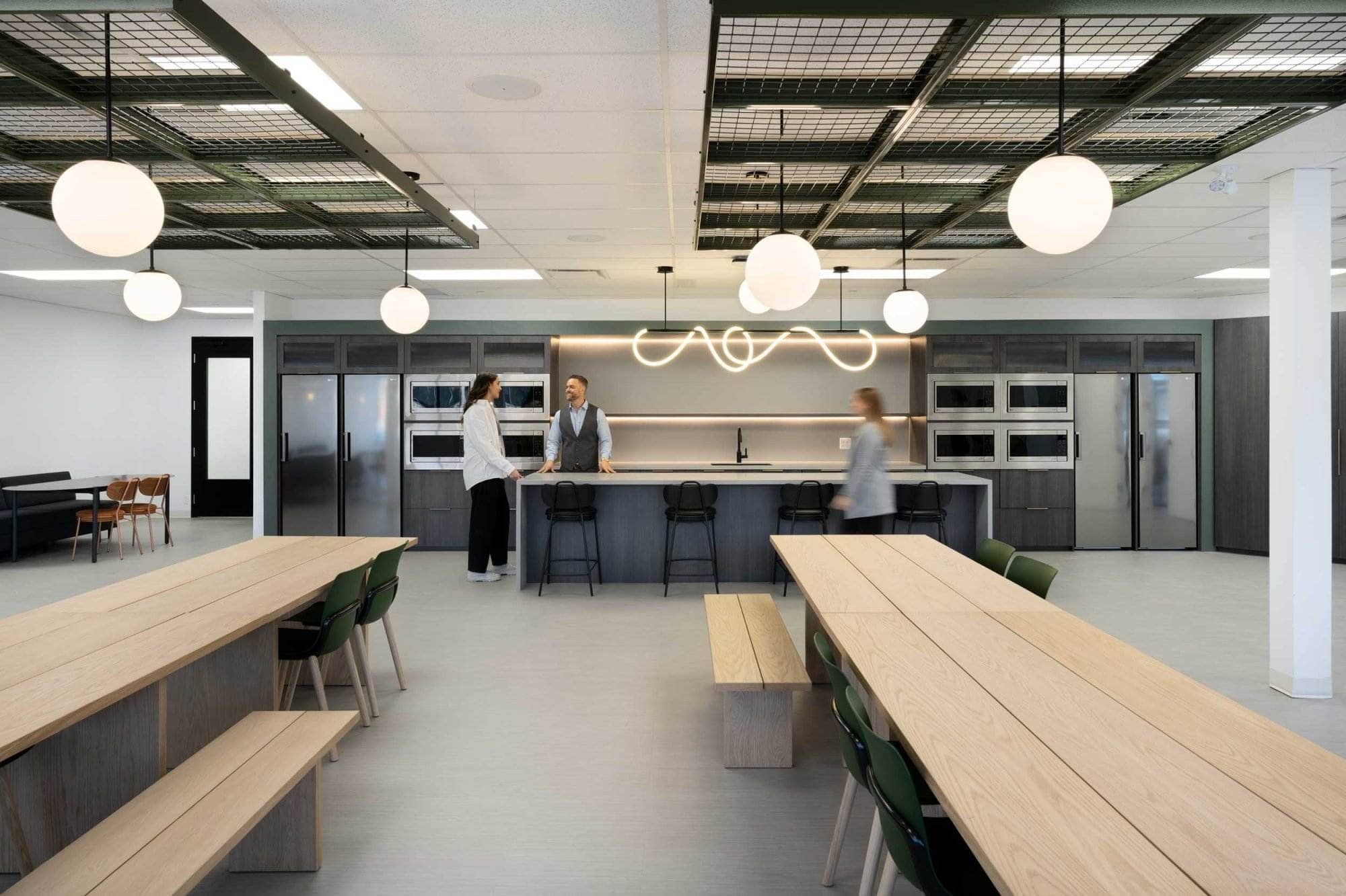 Cuisine de bureau et salle à manger modernes avec tables en bois, suspensions et personnes engagées dans une conversation sur un aperçu de l'entreprise.
