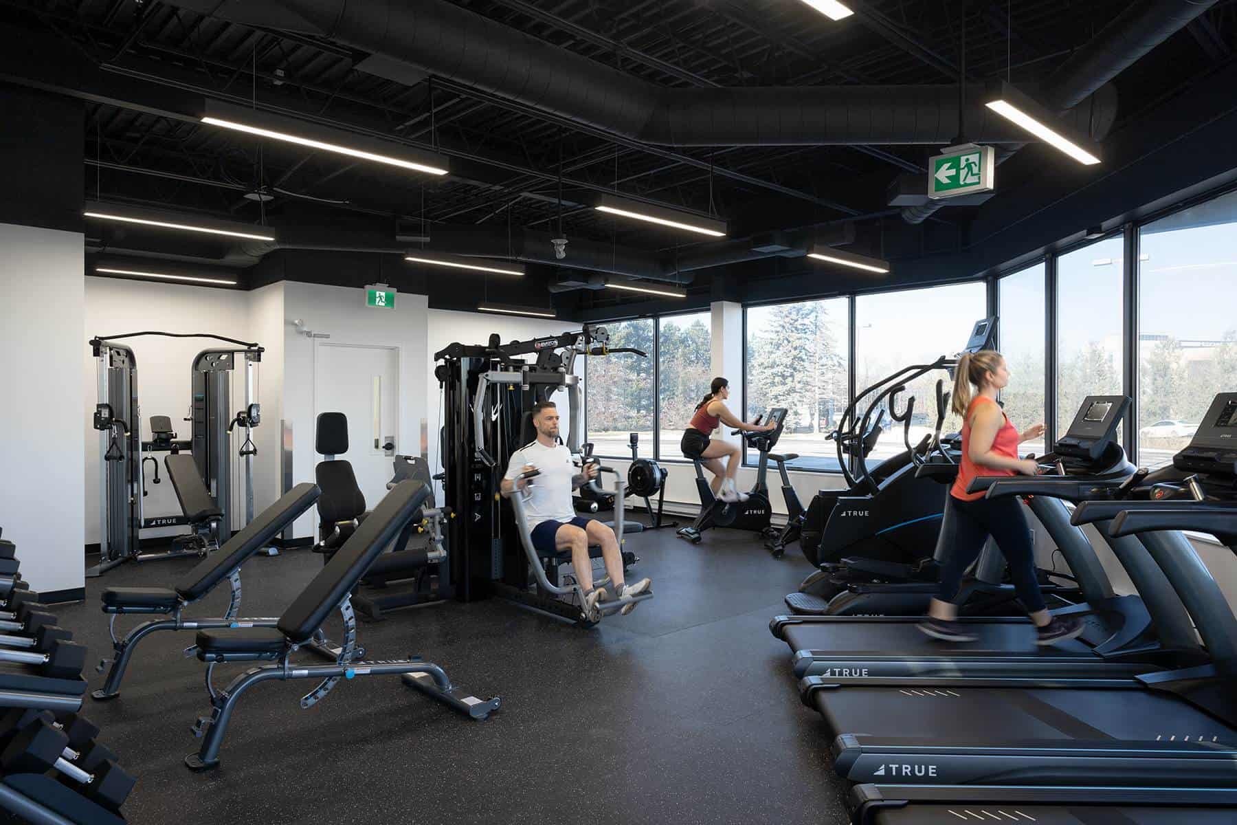 Intérieur d'une salle de sport moderne avec divers appareils d'exercice et personnes s'entraînant, y compris des tapis roulants et des stations de musculation, repensé pour une conception stratégique du lieu de travail afin d'améliorer le bien-être au travail.