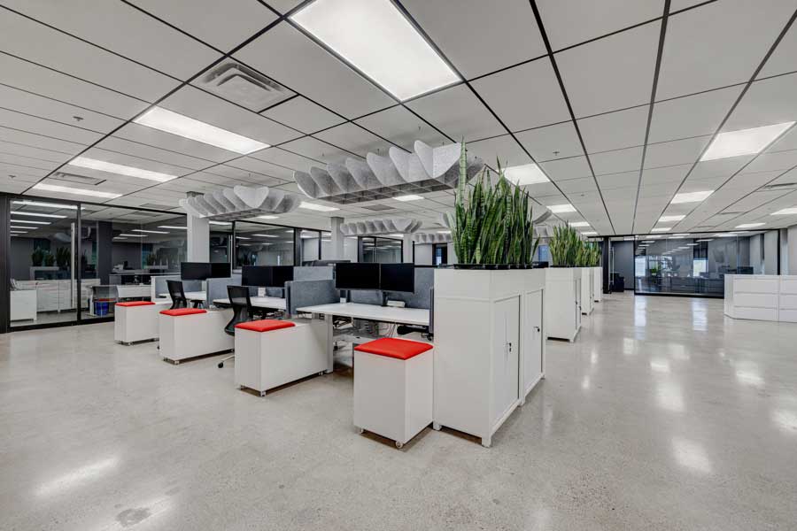 Espace de bureau moderne avec des cabines, des chaises rouges, des bureaux blancs et des plantes vertes, dot&eacute; d'un sol r&eacute;fl&eacute;chissant et d'un &eacute;clairage z&eacute;nithal dans le cadre d'une conception globale du lieu de travail.