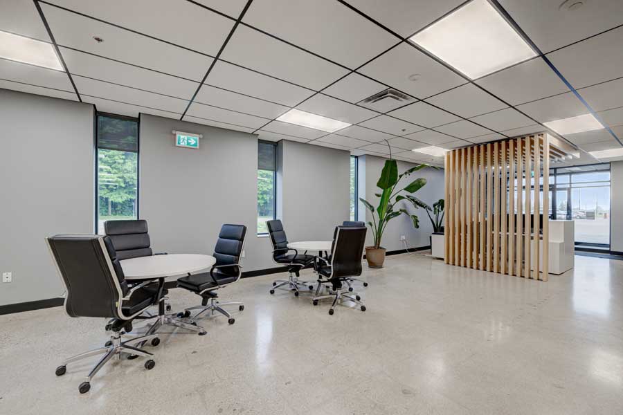 Salle de r&eacute;union de bureau moderne avec une table ronde, plusieurs chaises et une grande plante &agrave; c&ocirc;t&eacute; d'une cloison en bois, sous des plafonniers lumineux &mdash; optimis&eacute;e dans le cadre de la conception globale de notre lieu de travail.